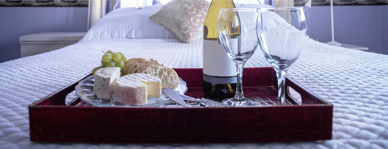 wood tray on a bed with wine and cheese